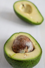 Macro top view of two half avocados with seed, selective focus, on white wooden table in vertical