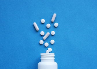 A pile of pills on a blue background. White pills fall out from a white jar on a blue background.
