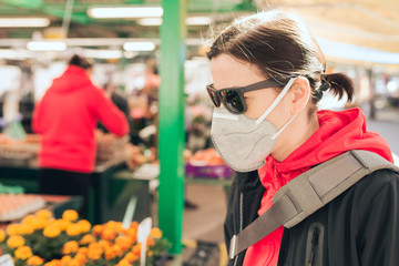 Woman with a protective mask on her face buying fresh flowers at a local market - Coronavirus...