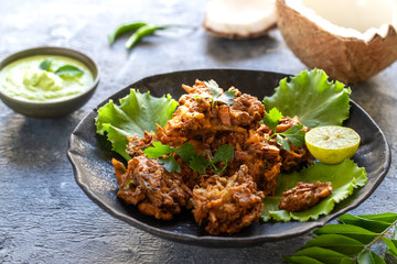 Indian cuisine Indian food. pakora traditional Indian deep-fried snack. pakoras on black plate with coconut chutney sauce curry leaves. national appetiser authentic vegetarian Asian food. travel food