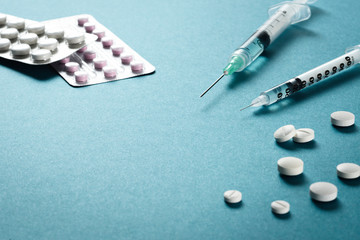 Two syringes with needles among tablets or medicine pills and medicine pack on a green surface....