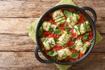 Italian cuisine zucchini rolls baked with ricotta cheese and herbs in tomato sauce in a pan close-up. horizontal top view