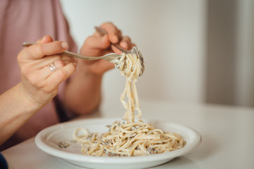 Young woman eats Italian pasta with mushrooms. Close-up spaghetti winds it around a fork with a...