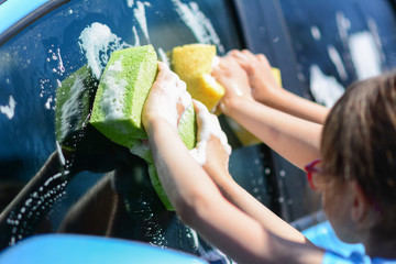 Closeup side view of a young girl washing car with sponge. Little girls washing car. Summer. Sunset.