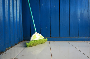 A green broom on a dirty floor  