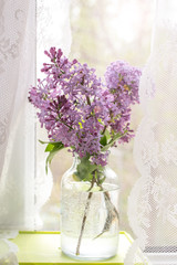 Bright blooms of spring lilacs on the window in house. Spring purple flowers close-up on the blurred background. Selected focus.