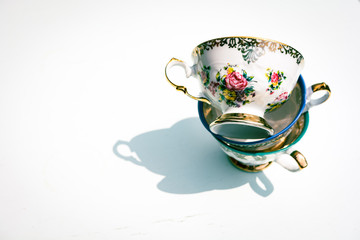 Stack of vintage porcelain tea cups with floral and golden decorations on white background. Concept...