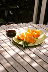 Red wine served outside in garden on white table with fresh orange in sun lights close up