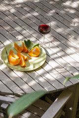Red wine served outside in garden on white table with fresh orange in sun lights close up
