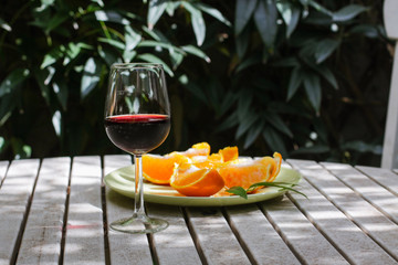 Red wine served outside in garden on white table with fresh orange in sun lights close up