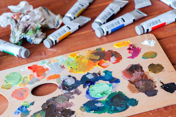 Close up oil painting process. Oil paints palette. Oil painting tools on the wooden table. Painter work place. Paint tubes.