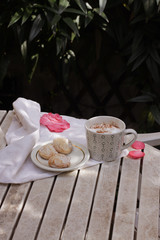 White porcelain cup of hot coffee, cappuccino with three Italian amaretti cookies.Summer breakfast in a terrace - coffee, amaretti and flowers