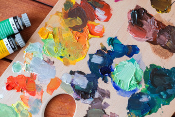 Close up oil painting process. Oil paints palette. Oil painting tools on the wooden table. Painter work place. Paint tubes.