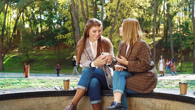 Amiable stylish girls browsing social media in beautiful park