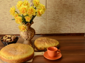 House. On the table there is a vase with a bouquet of fresh daffodils, delicious homemade pies, an orange cup and saucer.