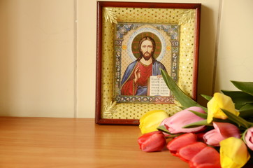Religion and culture. On the table is an icon of Jesus Christ, lies a beautiful bouquet of tulips.