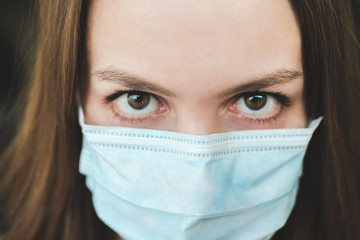 Sad girl in a medical protective mask and a yellow T-shirt looks at the camera close-up. Covid-19 coronavirus pandemic. Isolation at home. Protect yourself and your loved ones.