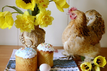 Religion and culture. Easter day. A decorative chicken sits on the table, there are festive cakes, a vase with beautiful yellow daffodils.