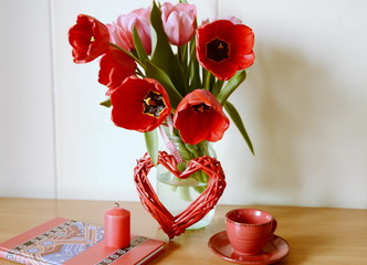 
Celebration. On the table is a vase with a bouquet of fresh beautiful tulips and a decorative red heart.