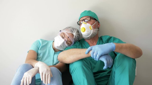 Tired doctor and nurse are resting sitting on the floor in a hospital corridor.