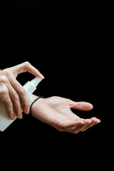 Male hand with a sanitizer spray disinfect his hand in the house on a black background. Covid-19...