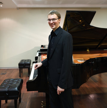 Young beautiful pianist in black suit near Grand piano