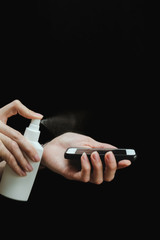 Male hand with a sanitizer spray disinfect the surface of the smartphone on black background. Covid-19 Coronavirus Quarantine Pandemic. Isolation at home. Protect yourself and your loved ones.