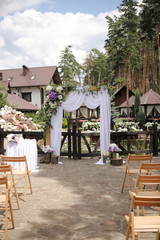 Fototapeta na wymiar Wedding decoration. Arch with white textile curtain and purple flower decor. Wooden elements. Outdoor wedding ceremony in the coniferous forest. Selective focus