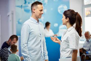 Obraz na płótnie Canvas Smiling man talking to a nurse in a hallway at medical clinic.
