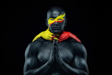 Fototapeta na wymiar Man with female hands on the body. Bodybuilder athlete with yellow face art and body paint. Colorful portrait of the guy with bodyart.
