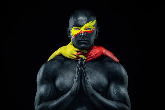 Man with female hands on the body. Bodybuilder athlete with yellow face art and body paint. Colorful portrait of the guy with bodyart.