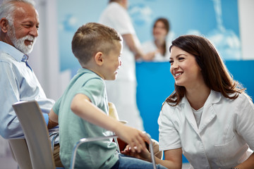 Happy female doctor communicating with small boy at hospital waiting room.