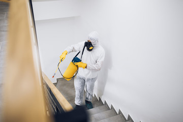 Exterminator in work wear spraying pesticide with sprayer.