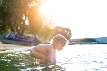 Cute adorable cheerful caucasian little blond toddler boy enjoy having fun playing at lake or river...
