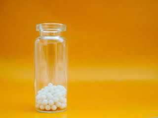 Homeopathic globules and glass bottle on yellow background. Homeopathic Medicine