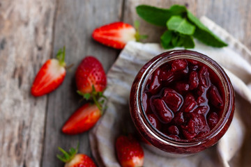 Strawberry jam in a glass jar with some fresh strawberry on wooden old rustic table. Homemade strawberry marmelade and fruits. Selective focus. Top view