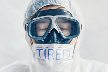 Inspiring doctor or virologist bio suit and protective mask with the inscription Tired.