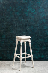 High white wooden stool on a blue green plaster wall background wiht copy space vertical. Bar chair...
