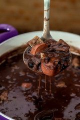 hand holding spoon with brazilian feijoada. 