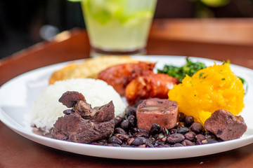 brazilian feijoada on white plate. Accompanied by rice, sausage, cabbage, pastry and caipirinha