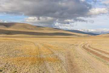 Fototapeta na wymiar Mongolia landscape. Winding dirt road through lush rolling hills of Central Mongolian steppe. Mongolian Altai