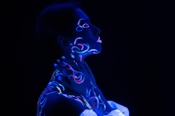 fantastic unusual shot of young caucasian woman with fluorescent make-up glowing in ultra-violet light. body art on attractive woman, unusual colorful design