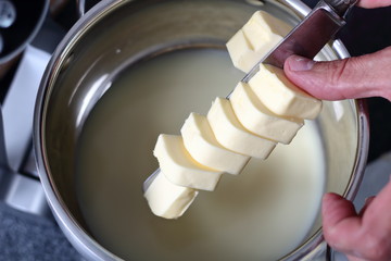 Fototapeta na wymiar Adding diced butter into pan with sweetened condensed milk. Making Boston Banoffee Pie.