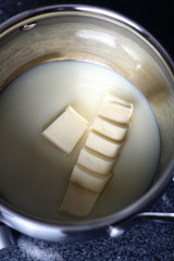 Adding diced butter into pan with sweetened condensed milk. Making Boston Banoffee Pie.
