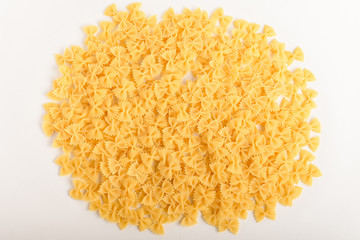 Heap of dried Farfalle Rigate traditional Italian pasta ready to be cooked, isolated on a white table, top view or flat lay of healthy food 
