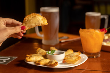 Hand hold fried pastry. Brazilian snack served on white plate accompanied by chopp beer.