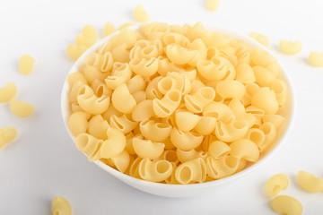 Many dried cornetti rigati traditional Italian pasta in a white bowl ready to be cooked, isolated on a white table, top view or flat lay of healthy food 
