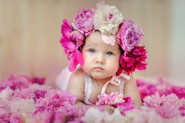 Cheerful smiling little girl on a background with pink peonies. Cute baby girl wearing wreath....