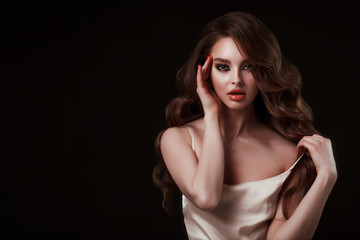 Naklejka premium Beauty portrait of elegant young woman. Glamour makeup. Face of the beautiful woman with long brown curly hair posing at studio over dark background. Sensual portrait.