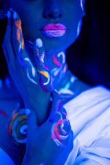 young caucasian fashion model with fluorescent prints on skin, attractive girl posing at camera, bright lines on her skin glows in ultra violet light. isolated black background